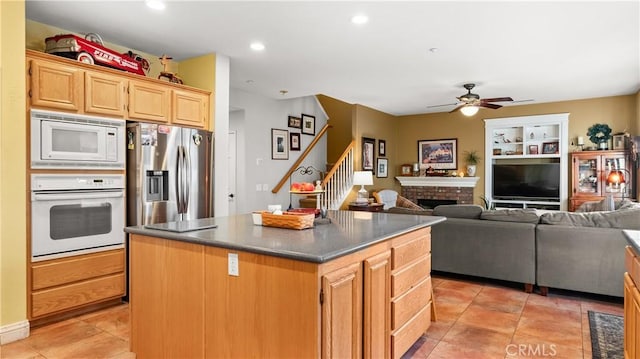 kitchen with light brown cabinets, white appliances, open floor plan, a center island, and dark countertops