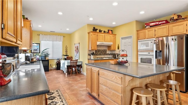 kitchen with a center island, dark countertops, a sink, white appliances, and under cabinet range hood