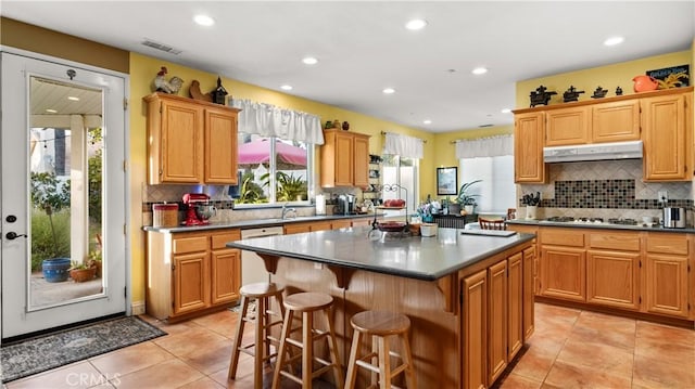 kitchen with a center island, light tile patterned floors, visible vents, stainless steel gas stovetop, and under cabinet range hood