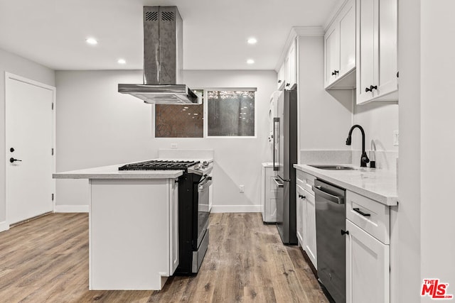 kitchen with appliances with stainless steel finishes, white cabinetry, island range hood, light hardwood / wood-style flooring, and sink