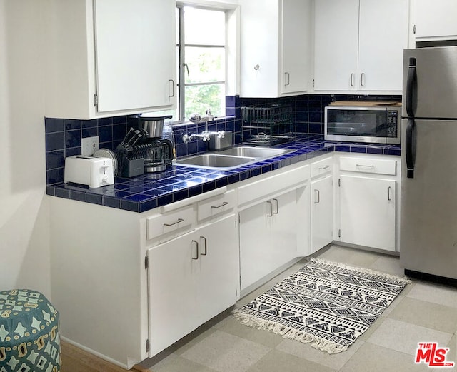 kitchen featuring tasteful backsplash, sink, white cabinets, stainless steel appliances, and tile countertops