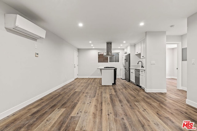 kitchen featuring white cabinetry, hardwood / wood-style flooring, appliances with stainless steel finishes, a center island, and a wall unit AC