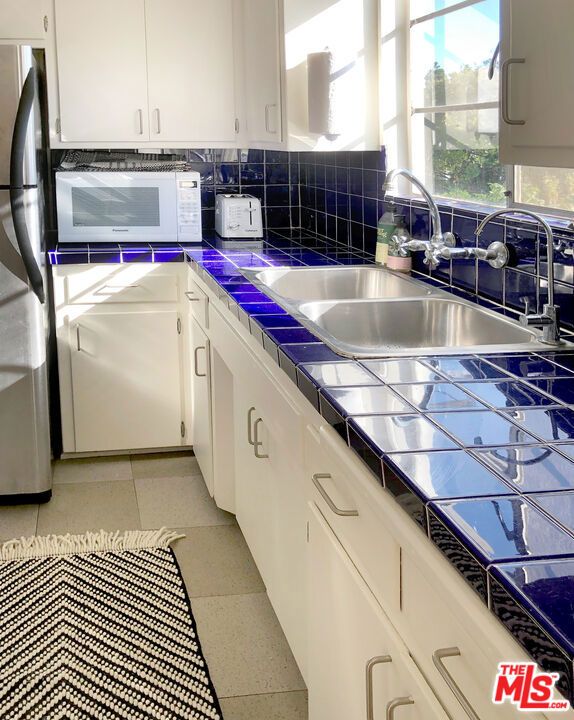 kitchen featuring tile counters, sink, stainless steel fridge, and white cabinets