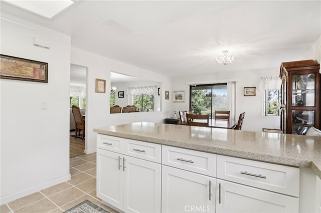 kitchen with an inviting chandelier, light stone countertops, light tile patterned floors, and white cabinets