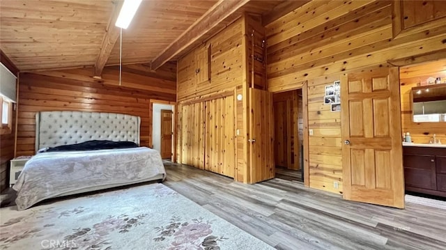 unfurnished bedroom with ensuite bathroom, light hardwood / wood-style flooring, lofted ceiling with beams, and wood walls