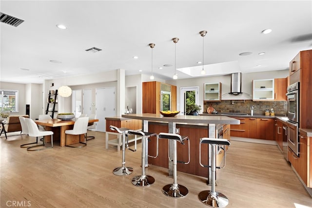 kitchen with wall chimney range hood, a breakfast bar, pendant lighting, light hardwood / wood-style floors, and double oven