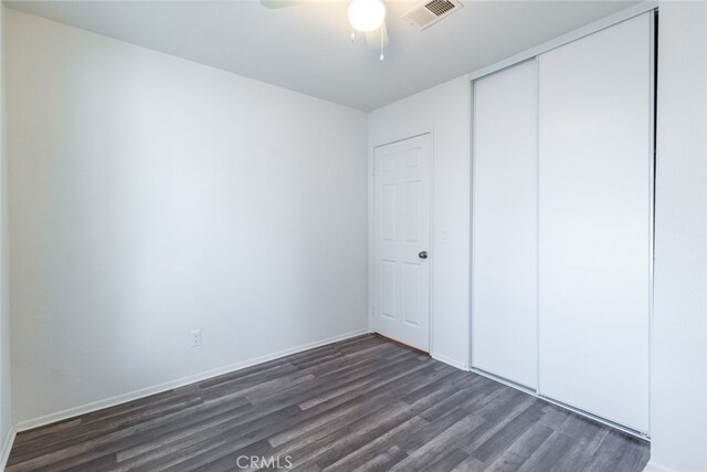 unfurnished bedroom featuring ceiling fan, a closet, and dark wood-type flooring