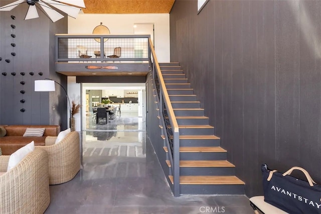 staircase with ceiling fan, concrete flooring, and wood walls