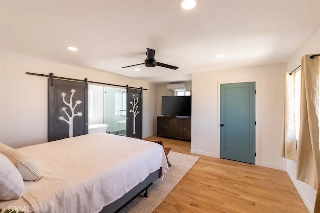 bedroom featuring ceiling fan, a barn door, a wall mounted air conditioner, light hardwood / wood-style floors, and ensuite bath