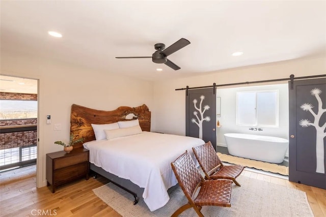 bedroom featuring a barn door, light wood-type flooring, and ceiling fan