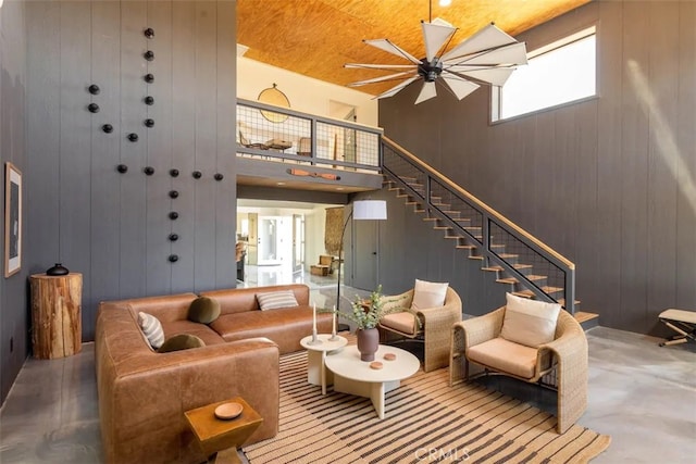 living room featuring wooden walls, wooden ceiling, concrete flooring, a towering ceiling, and ceiling fan