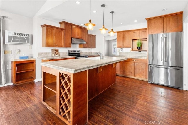 kitchen featuring a wall mounted air conditioner, dark wood-type flooring, a center island with sink, decorative light fixtures, and stainless steel appliances