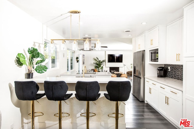 kitchen with dark wood-type flooring, stainless steel fridge with ice dispenser, built in microwave, decorative light fixtures, and white cabinetry