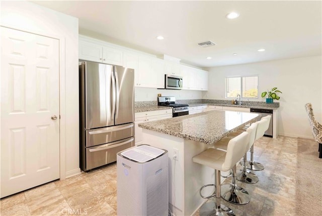 kitchen with light stone countertops, a center island, stainless steel appliances, white cabinets, and sink