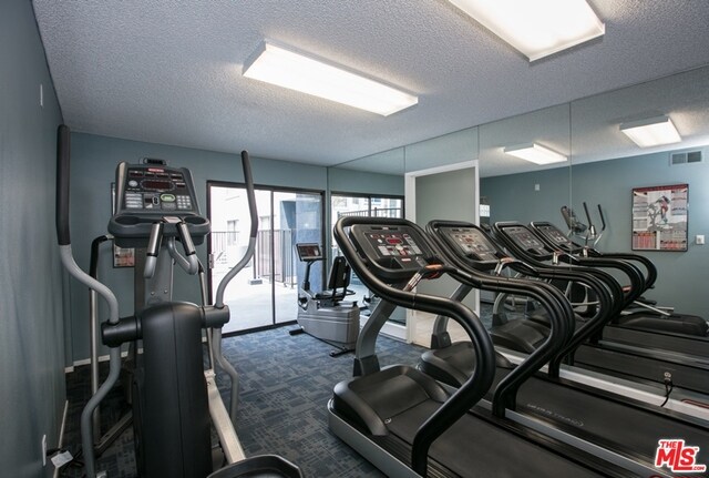 workout area featuring a textured ceiling and dark carpet