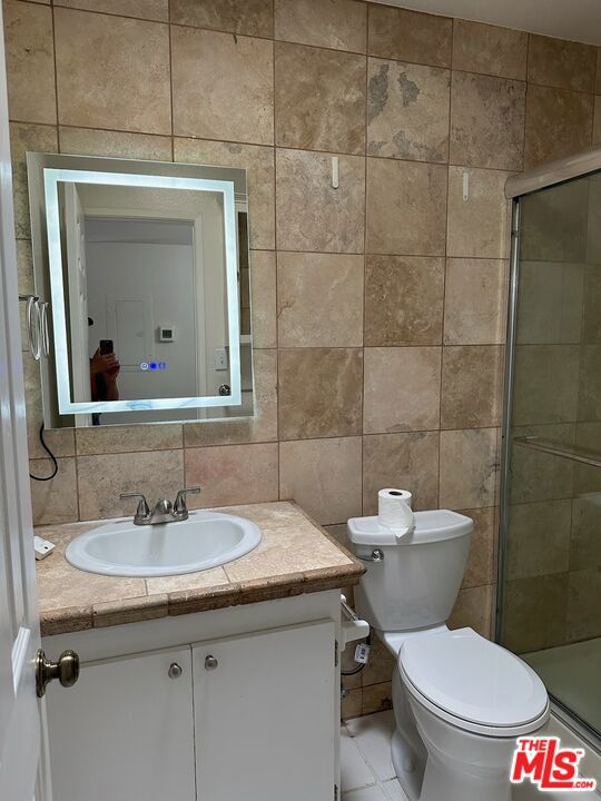 bathroom featuring vanity, an enclosed shower, and tile walls