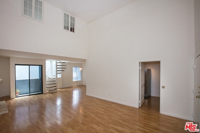 unfurnished living room featuring a towering ceiling, wood-type flooring, and ornamental molding