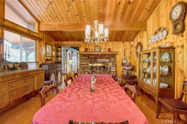 dining room with an inviting chandelier, light wood-type flooring, wooden walls, beamed ceiling, and a fireplace