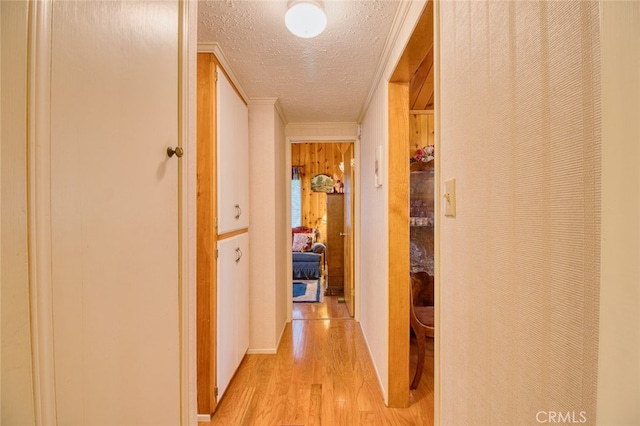 corridor with ornamental molding, a textured ceiling, and light wood-type flooring