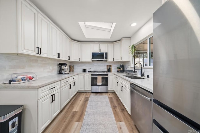 kitchen with appliances with stainless steel finishes, light wood-type flooring, a skylight, sink, and white cabinetry