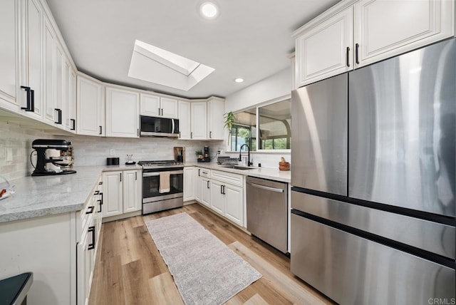 kitchen with light wood-type flooring, tasteful backsplash, a skylight, stainless steel appliances, and white cabinetry