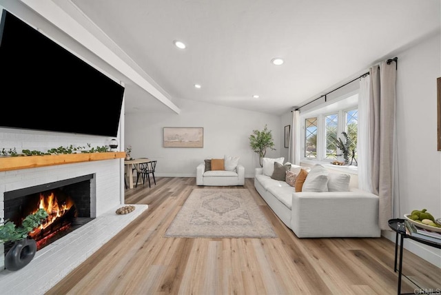 living room featuring a brick fireplace, light hardwood / wood-style floors, and vaulted ceiling