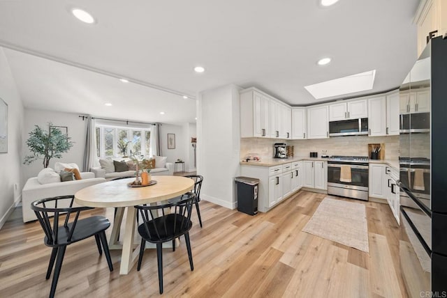 kitchen with light wood-type flooring, stainless steel appliances, white cabinetry, and a skylight