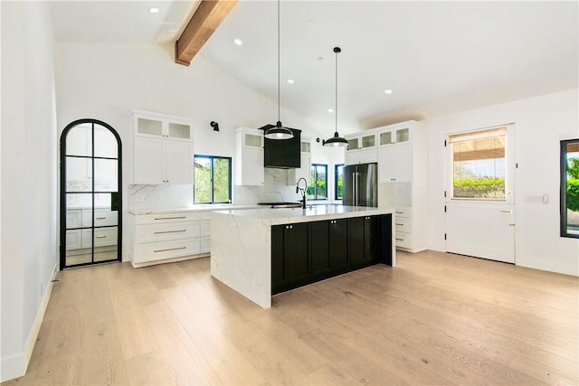 kitchen with pendant lighting, white cabinets, an island with sink, beamed ceiling, and stainless steel refrigerator