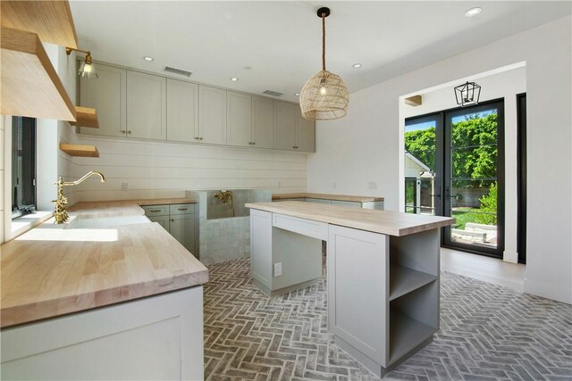 kitchen featuring pendant lighting, wooden counters, sink, gray cabinets, and a kitchen island