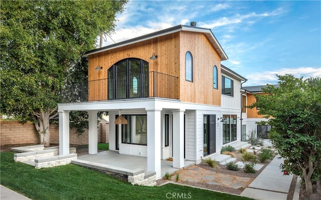 back of house with a balcony, fence, a lawn, and a patio