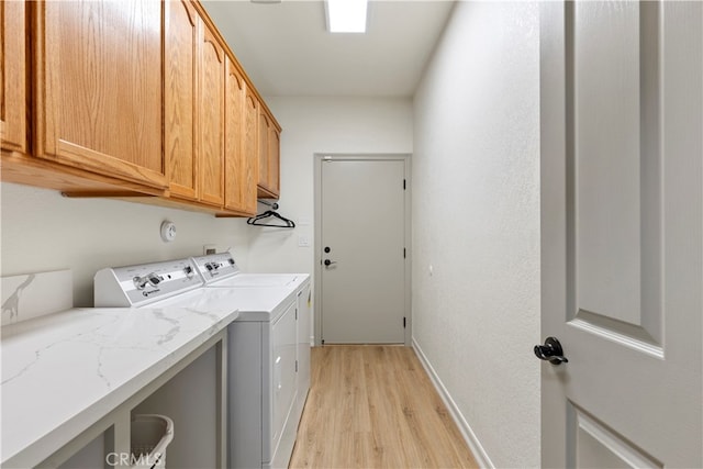 clothes washing area with light hardwood / wood-style floors, washing machine and clothes dryer, and cabinets