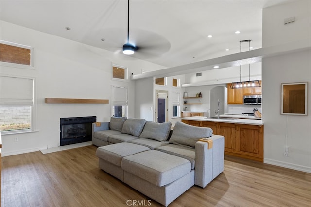 living room featuring light hardwood / wood-style flooring, a high ceiling, ceiling fan, and sink