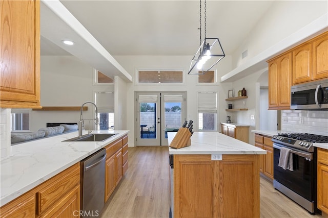 kitchen featuring appliances with stainless steel finishes, pendant lighting, light wood-type flooring, a center island, and sink