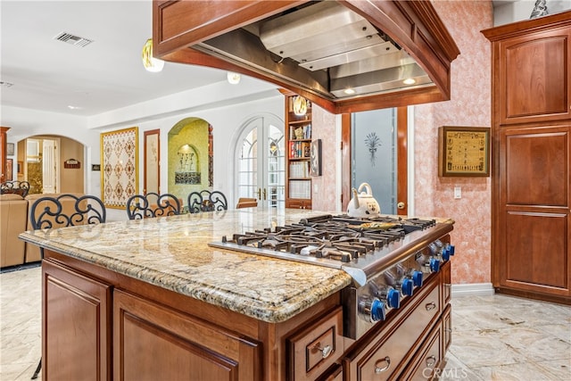 kitchen featuring stainless steel gas cooktop, a breakfast bar area, light stone counters, and custom exhaust hood