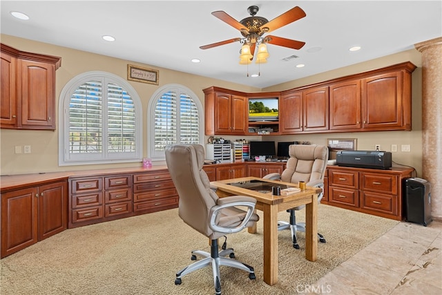 carpeted office space with built in desk, ornate columns, and ceiling fan