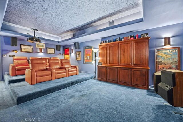 carpeted cinema room with a textured ceiling and a tray ceiling