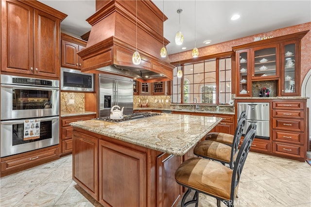 kitchen featuring custom range hood, a kitchen island, hanging light fixtures, built in appliances, and light stone counters