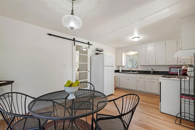 kitchen with white appliances, sink, a barn door, white cabinets, and light hardwood / wood-style floors