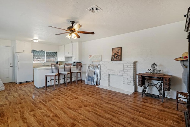 living room featuring ceiling fan, a fireplace, dark wood-type flooring, and a textured ceiling