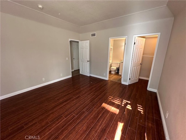 unfurnished bedroom with dark hardwood / wood-style flooring, a spacious closet, and connected bathroom