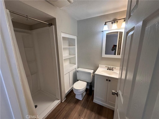 bathroom with vanity, toilet, a textured ceiling, walk in shower, and wood-type flooring