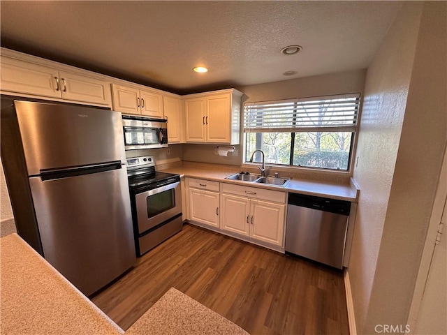 kitchen featuring wood finished floors, stainless steel appliances, light countertops, white cabinetry, and a sink