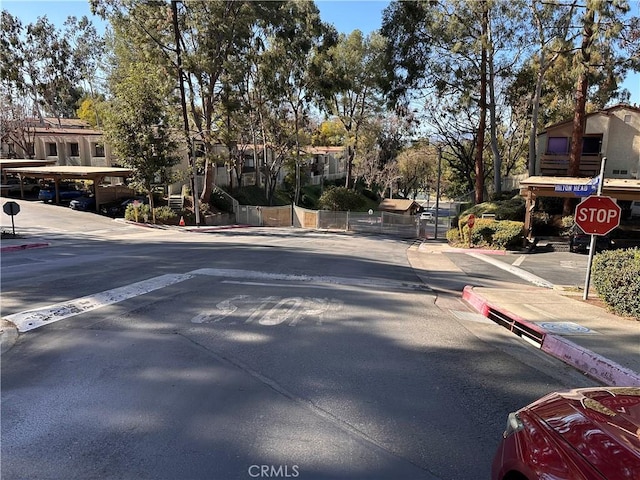 view of road featuring traffic signs, a gate, curbs, and sidewalks