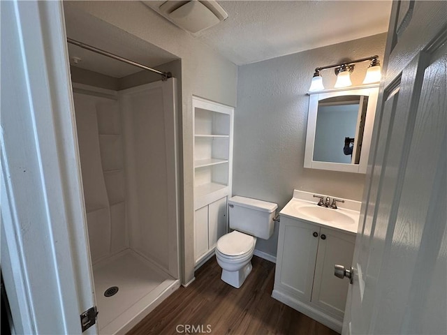 bathroom with a stall shower, a textured wall, toilet, wood finished floors, and vanity