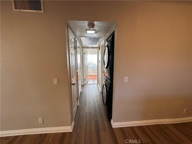 hallway with a textured ceiling, dark wood-style flooring, visible vents, baseboards, and stacked washer and clothes dryer