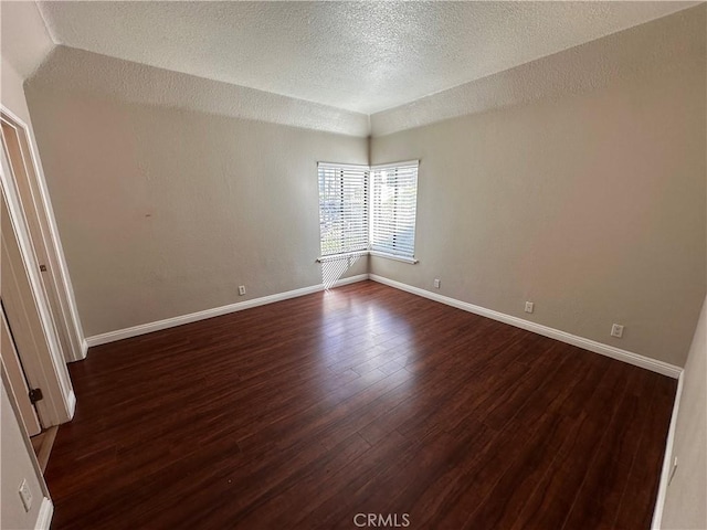 empty room with dark wood-style floors, a textured ceiling, and baseboards