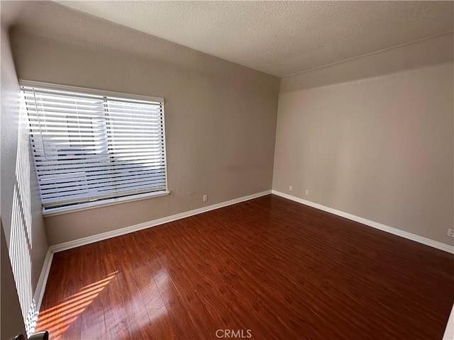 spare room with dark wood-style floors, a textured ceiling, and baseboards