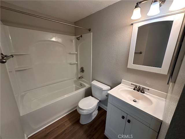 full bathroom featuring a textured wall, toilet, wood finished floors, vanity, and shower / washtub combination