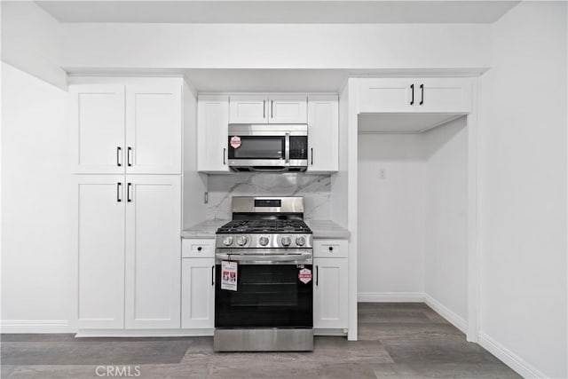 kitchen with appliances with stainless steel finishes, white cabinetry, wood-type flooring, decorative backsplash, and light stone counters