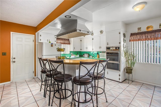 kitchen with a breakfast bar, white cabinets, island exhaust hood, backsplash, and light tile patterned floors